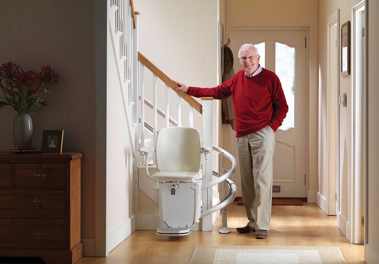 Man in red sweater standing next to curved stair lift