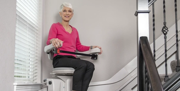 Woman in a pink shirt sitting on a Bruno Elite curved stairlift